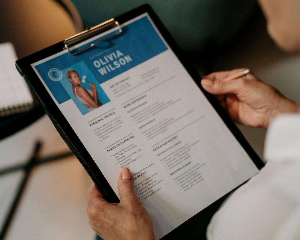 An HR professional reviews a resume on a clipboard during an office meeting.